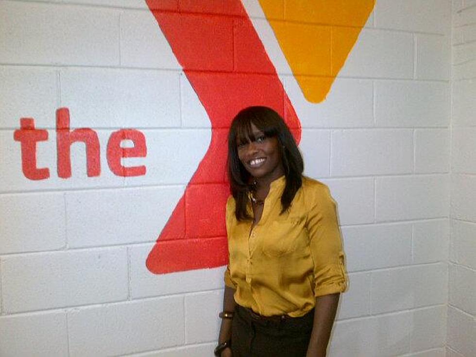 Woman in a yellow shirt smiling in front of a white brick wall with the YMCA logo painted on it