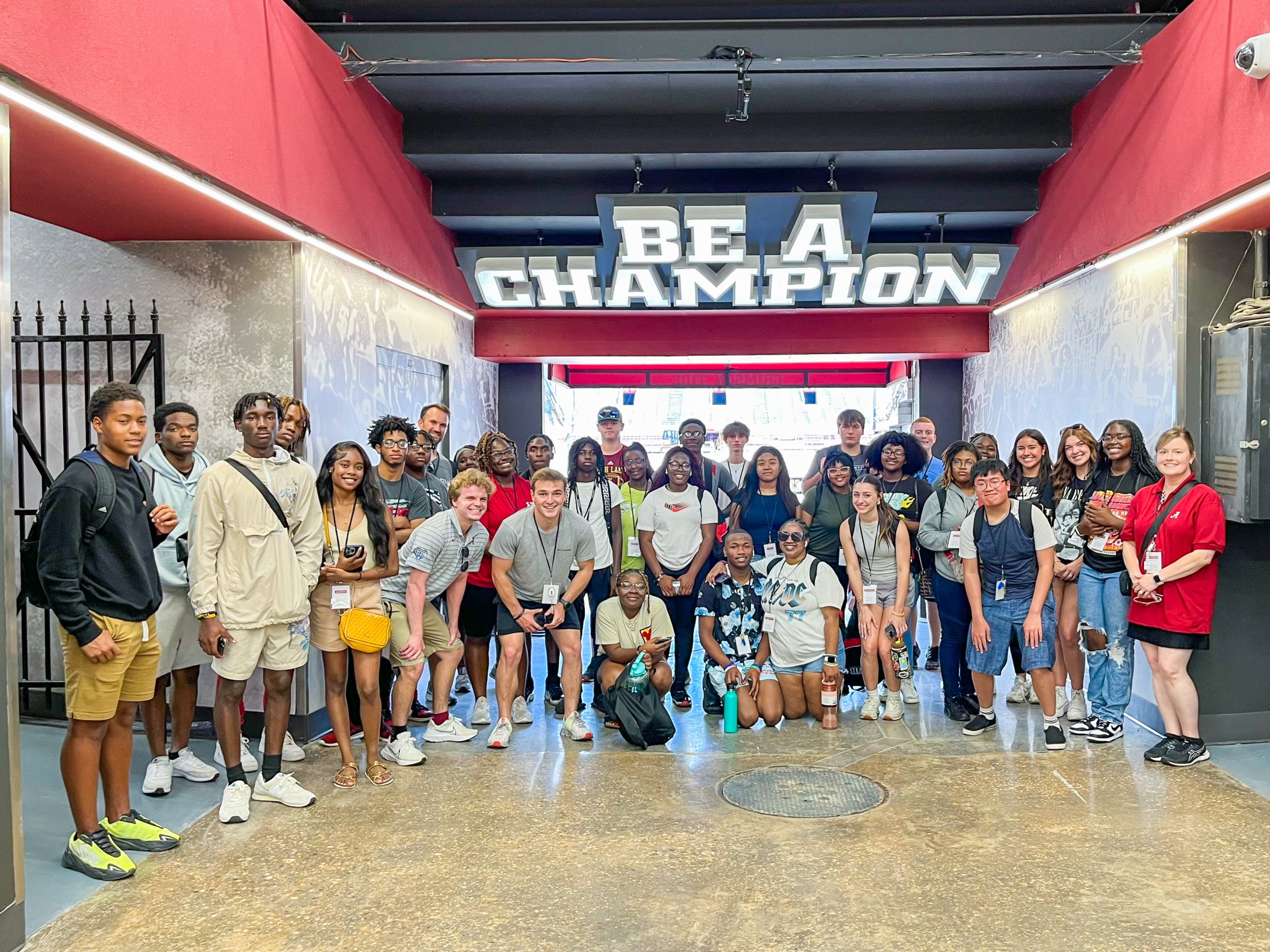 Large group of teenagers standing under a sign that says "Be a champion".