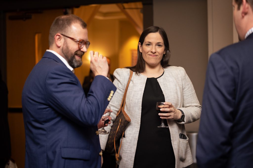 A woman and two men, dressed in business attire, talking while drinking waters