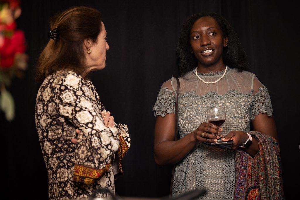 A woman in a pattern blouse listening to a woman in a gray lacy dress talk