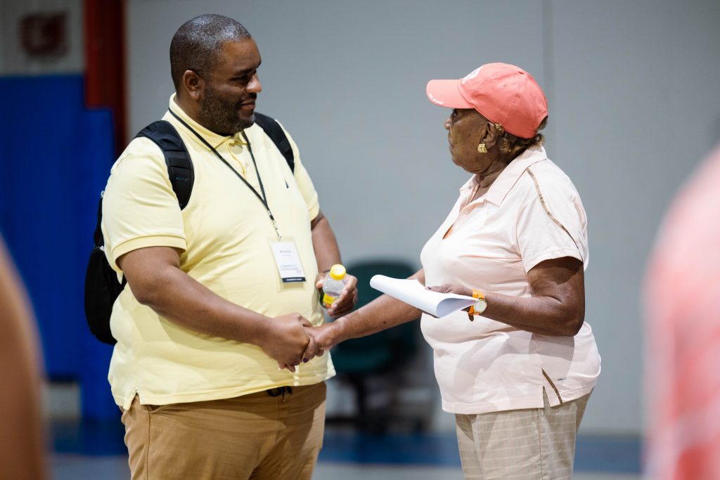 Man in a yellow shirt shaking hands with a woman in a pink cap