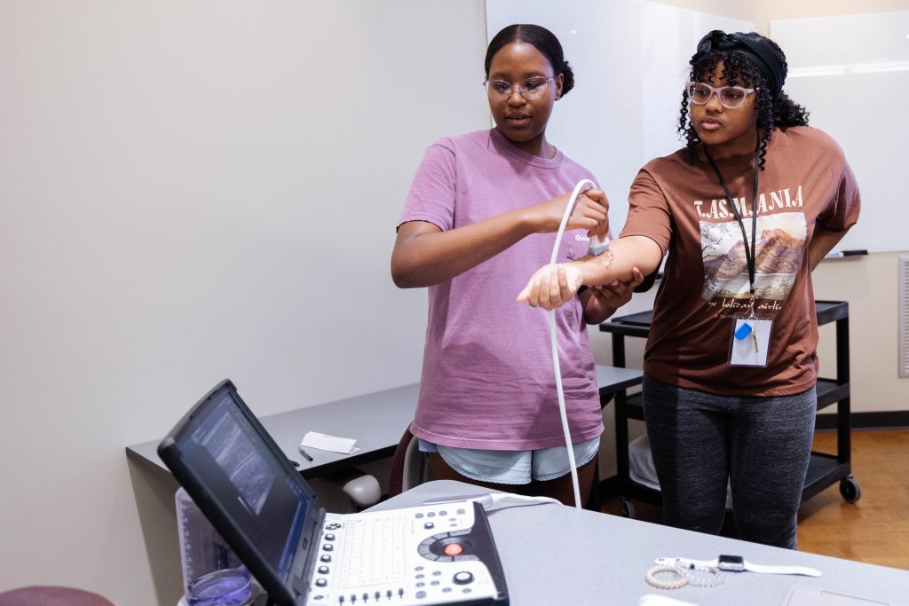 Two female students practicing an ultra sound on one of their arms