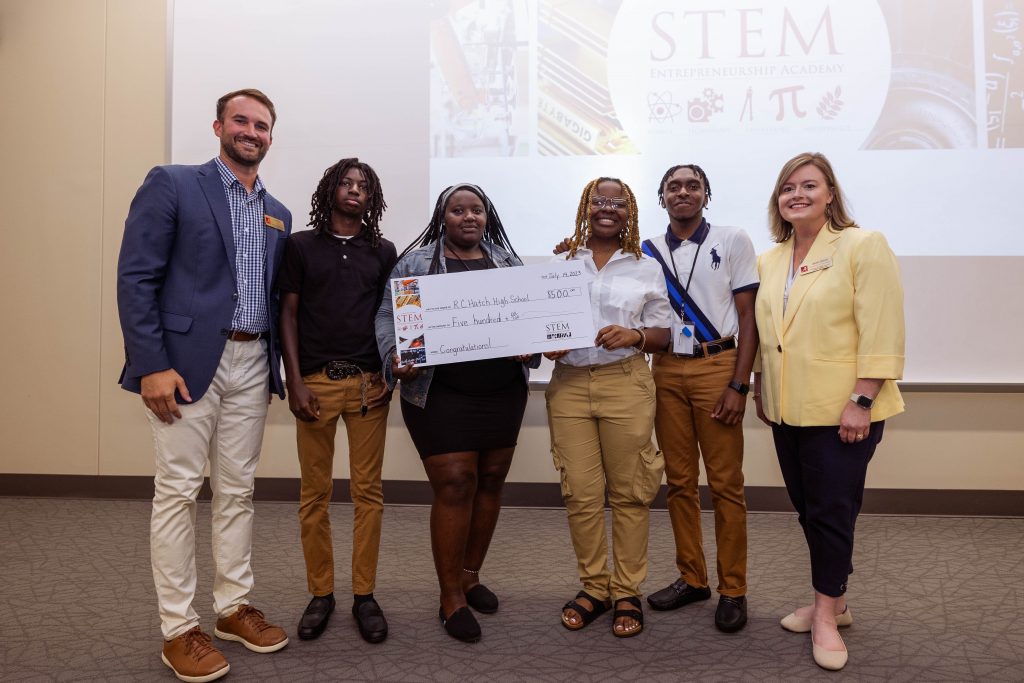 Group of men and women holding a large check in front of a STEM presentation