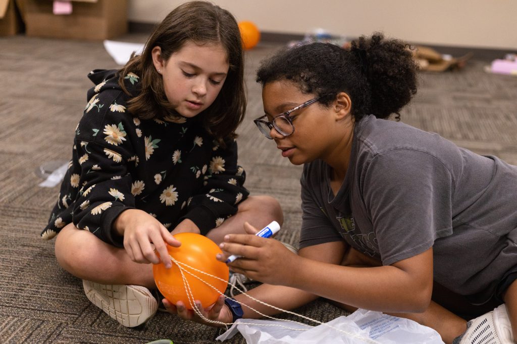 Two female kids working on a orange balloon