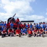 Group of students wearing blue and red shirts standing in front of a plane