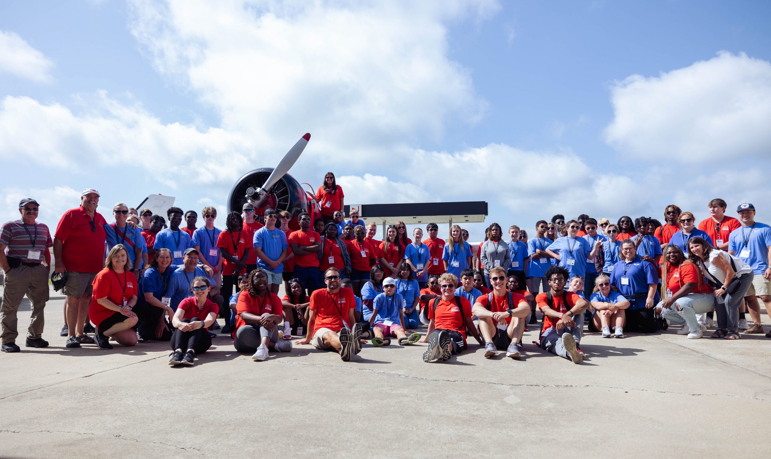 Group of students wearing blue and red shirts standing in front of a plane