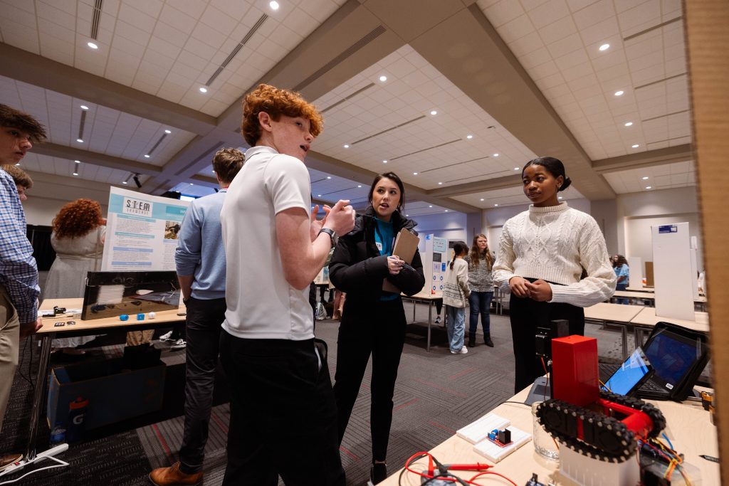 Red headed student discussing project with to  another female student and a judge