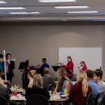 Students playing instruments while people are sitting at a table listening