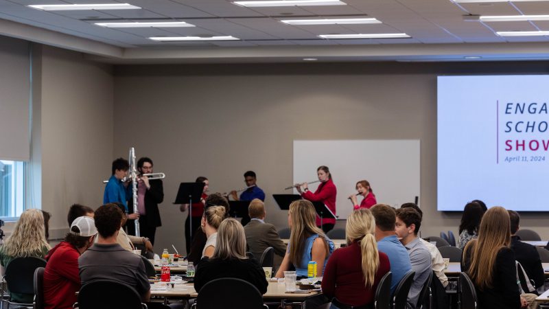 Students playing instruments while people are sitting at a table listening