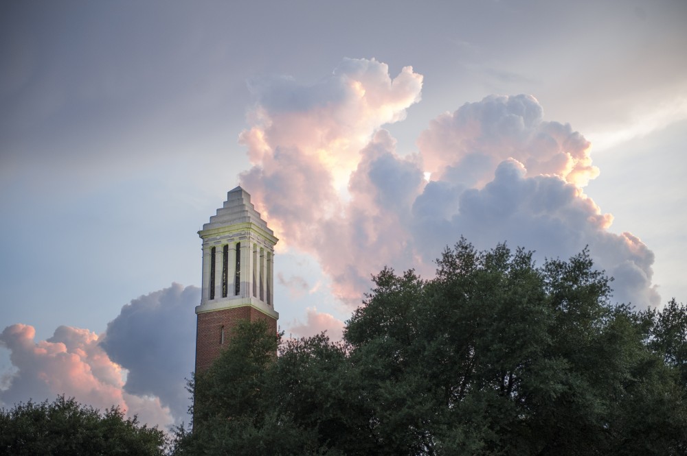 Campus bell tower with fluffy clouds lit by the sunset in the sky behind it