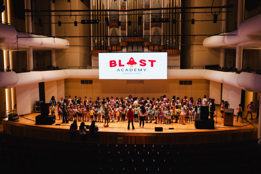 Large group of people standing on a stage underneath a digital screen with the logo for BLAST