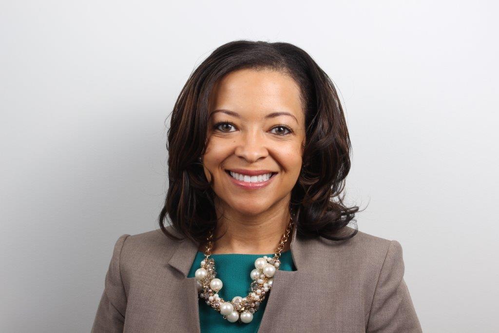 Headshot of Amber Bradford Buchanan wearing a gray blazer, aqua blouse, and graphic necklace