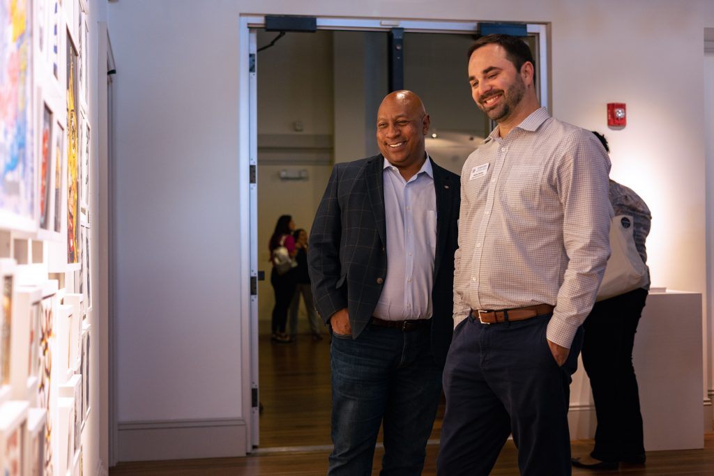 2 men looking at a wall of student made art