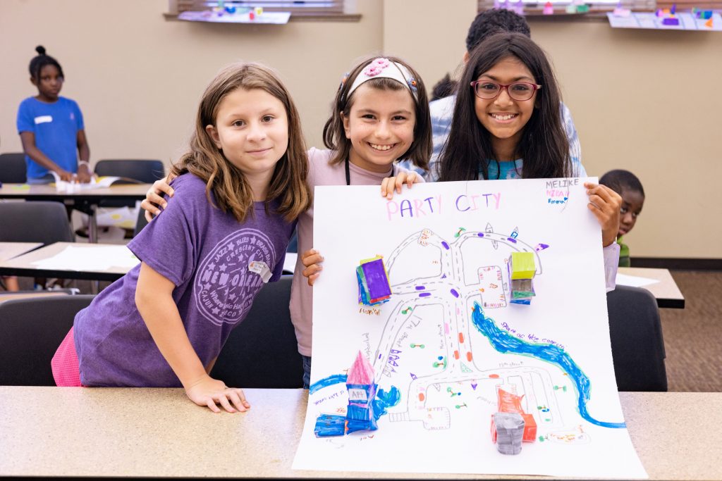 A group of young girls smiling and holding a hand drawn map