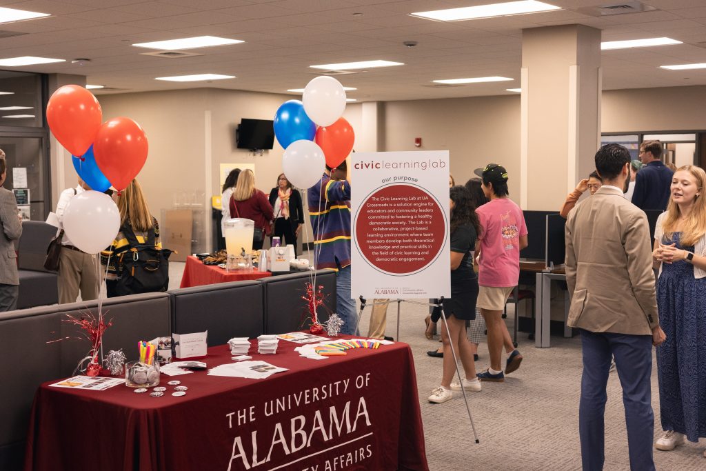 People mingling in a  room with a table and balloons