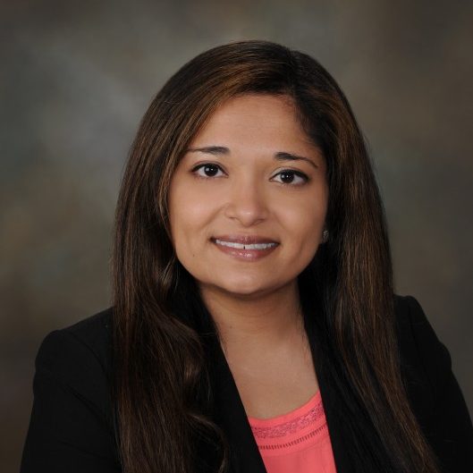 Headshot of Divya Patel wearing a black blazer and pink blouse