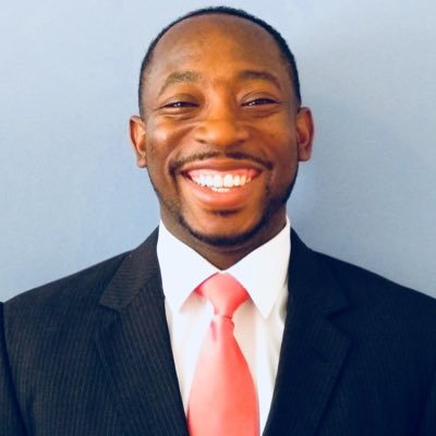 Headshot of Galvin Billups wearing a dark blue suit and a coral pink tie