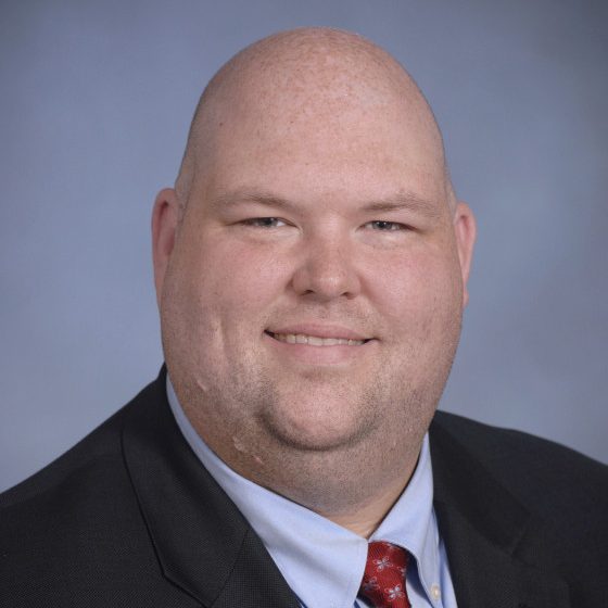 Headshot of Jonathan Adams wearing a dark suit with red tie