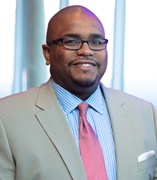 Headshot of Prince Cleveland wearing tan suit, blue shirt, and red tie