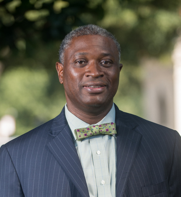 Headshot of Dr. Pruitt wearing a blue pinstripe suit and a green bowtie