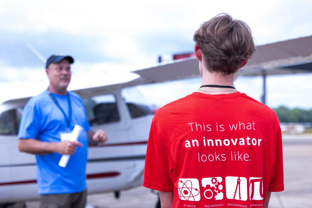 Image of the back of a guy's red t-shirt in front of a small airplane