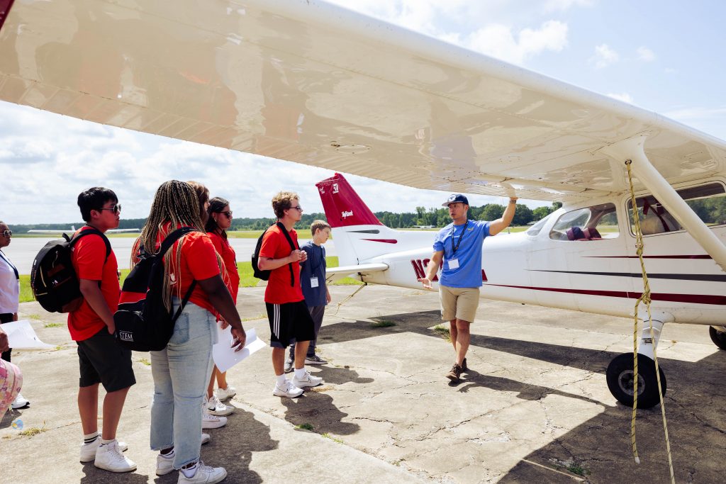 Group of students listening to a guide while standing underneath the wing of a plane