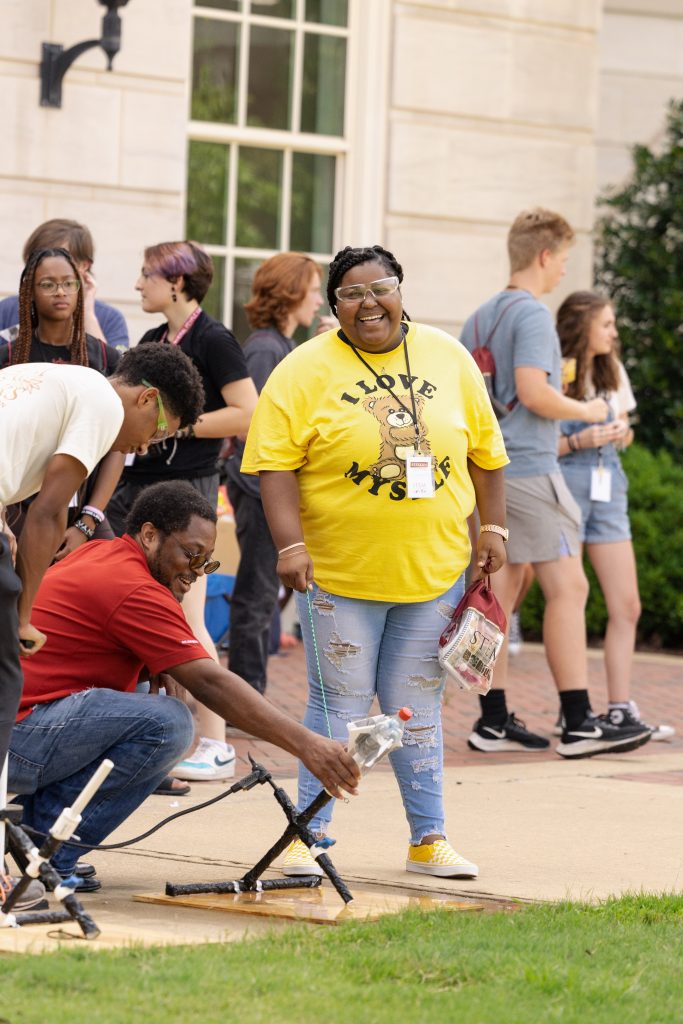 A small group of people gathered around a rocket made from a plastic soda bottle