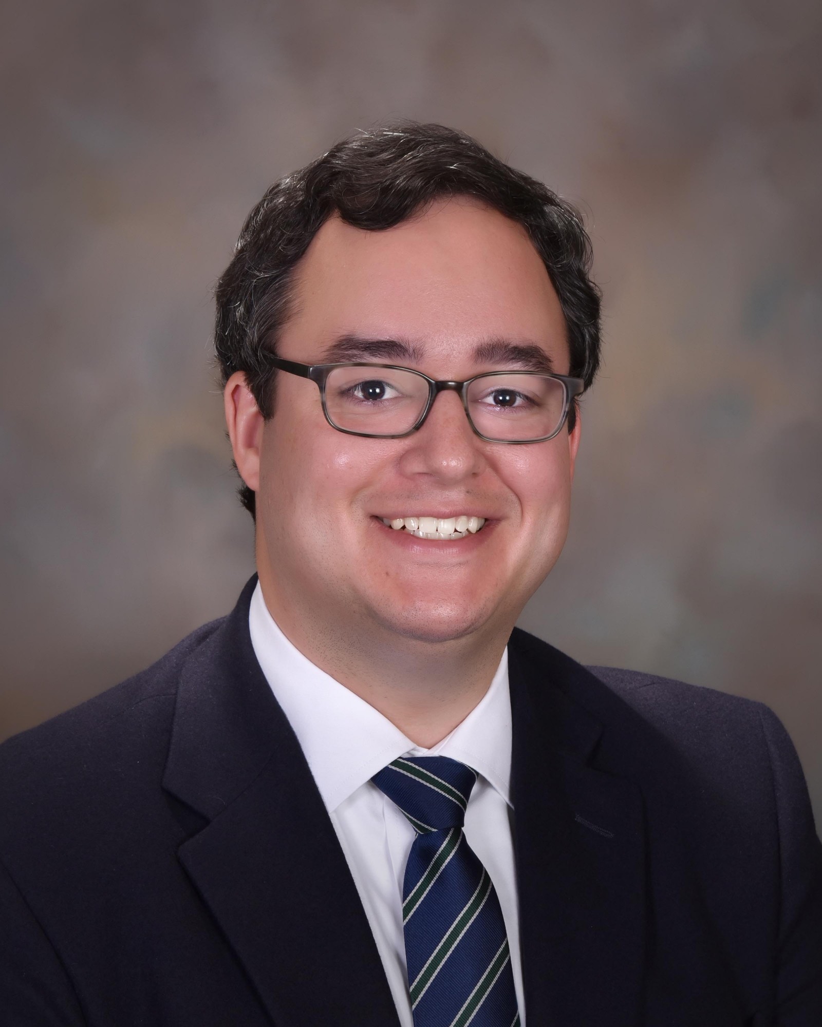 Headshot of Stephen McNair wearing a black suit and patterned tie