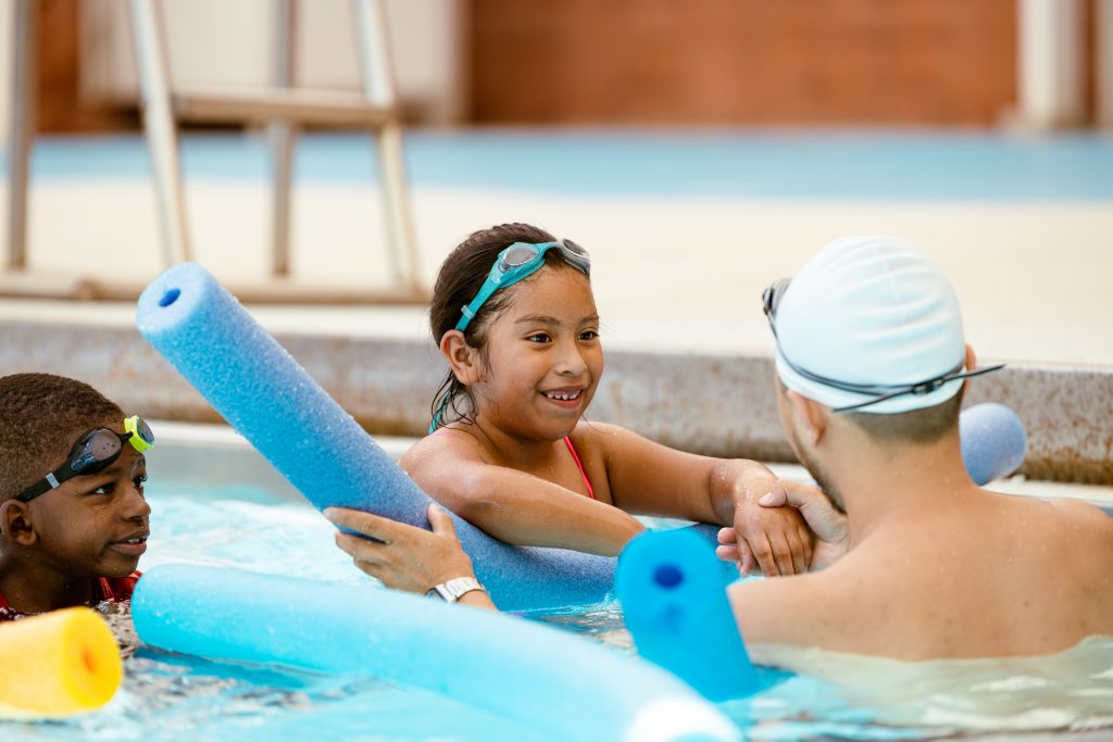 A young girl swims with an instructor in a pool