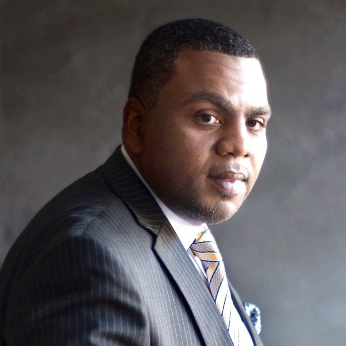 Headshot of Tyrell Jordan waring a dark suit and a patterned tie