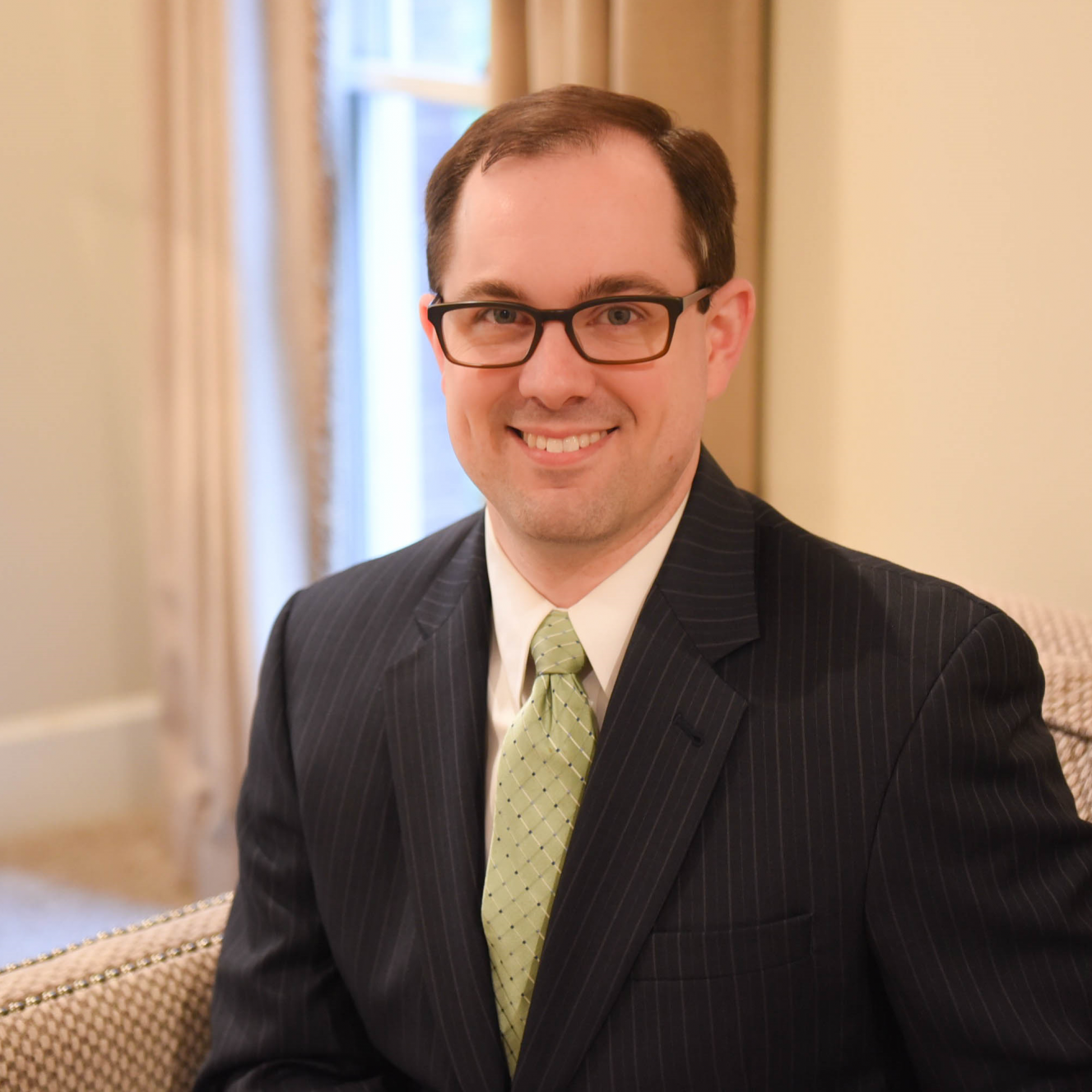 Headshot of Zac Riddle wearing a black suit and lime green tie