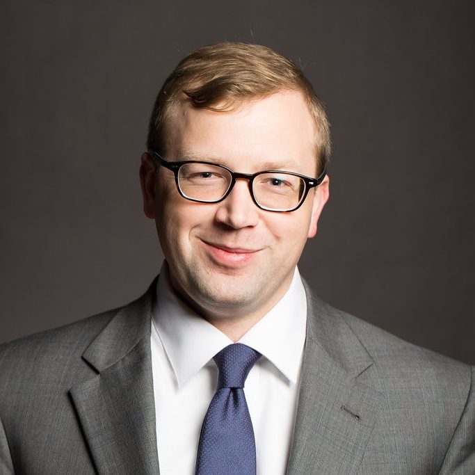 Headshot of Brandon Glover wearing a gray suit and blue tie