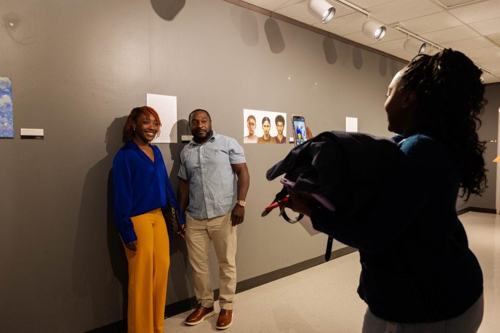 Two people standing near a hung piece of art at a gallery