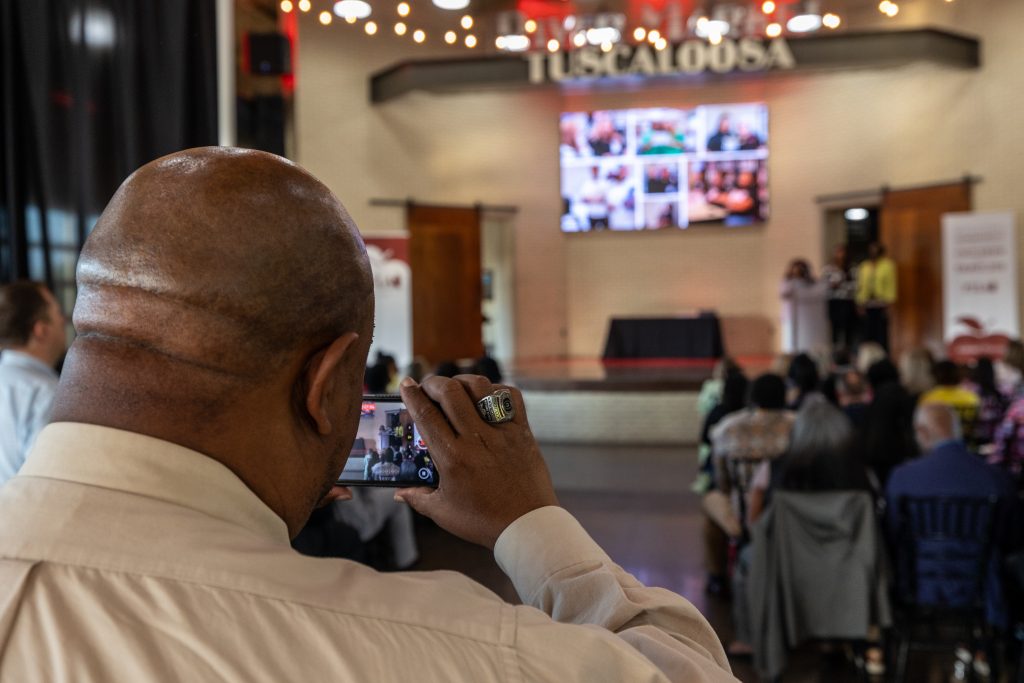 A man uses his phone to record video of the 2025 PTLA Graduation Ceremony at the Tuscaloosa River Market.